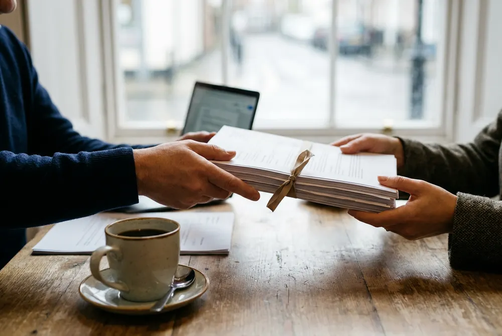 Accountant passing a bound set of finished annual accounts across the desk to a client