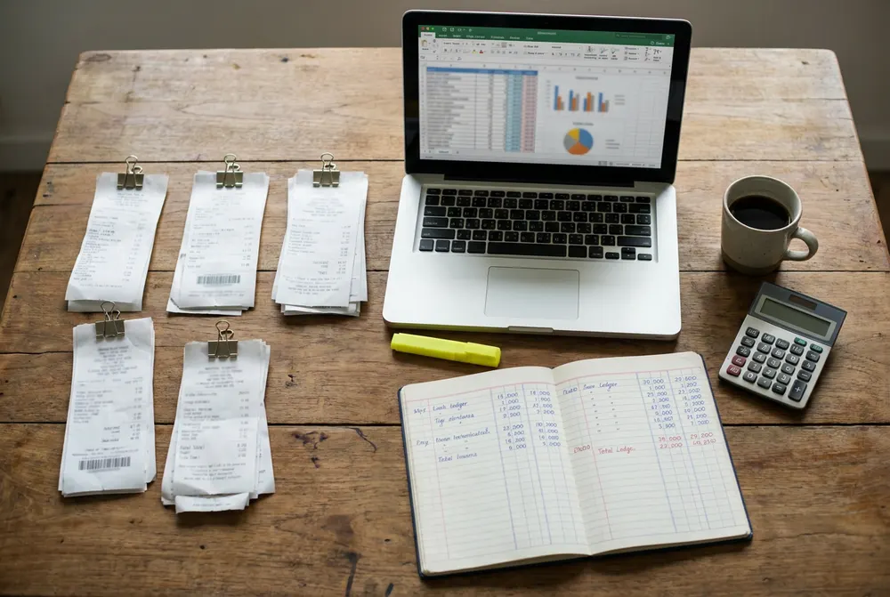 Desk with receipts clipped into piles beside a laptop, calculator and ledger