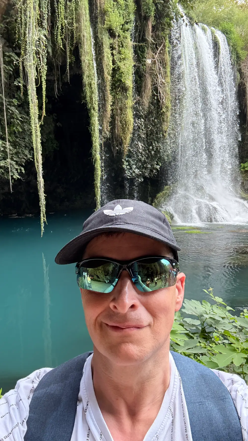 Mark Burtenshaw in a cap and sunglasses taking a selfie in front of a waterfall