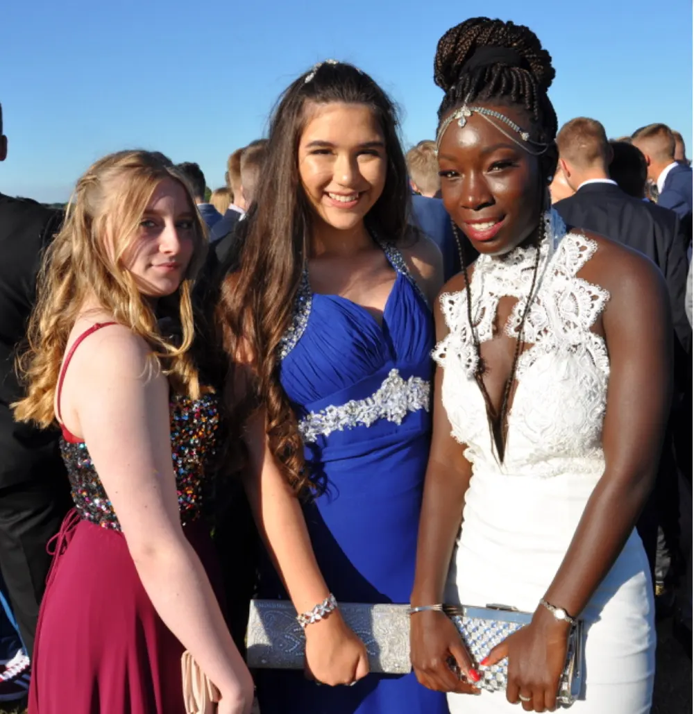 Three young women in evening dresses smiling together at an outdoor prom